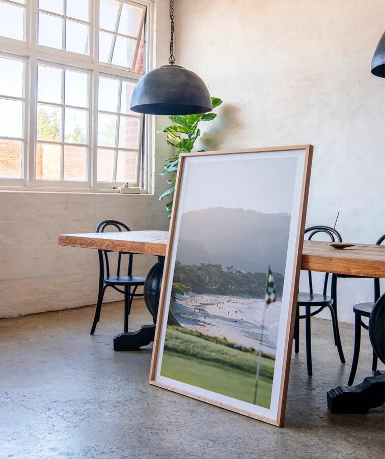 Framed coastal landscape print leaning against wall in minimalist interior