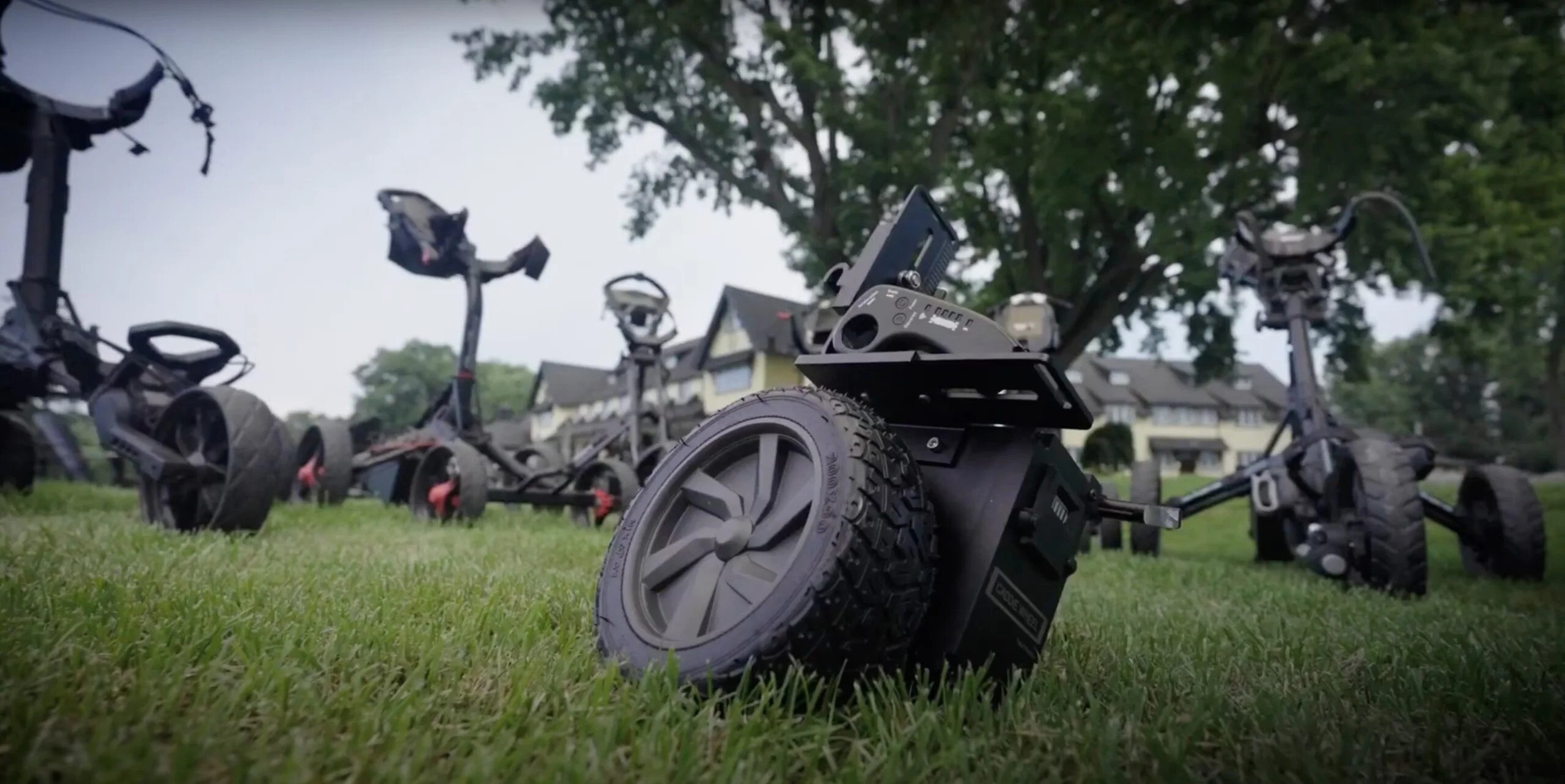 Robotic lawn mowers parked on grass with houses in background