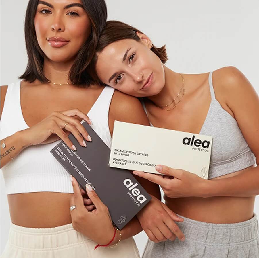 Two people holding Alea product boxes, wearing white and gray tops
