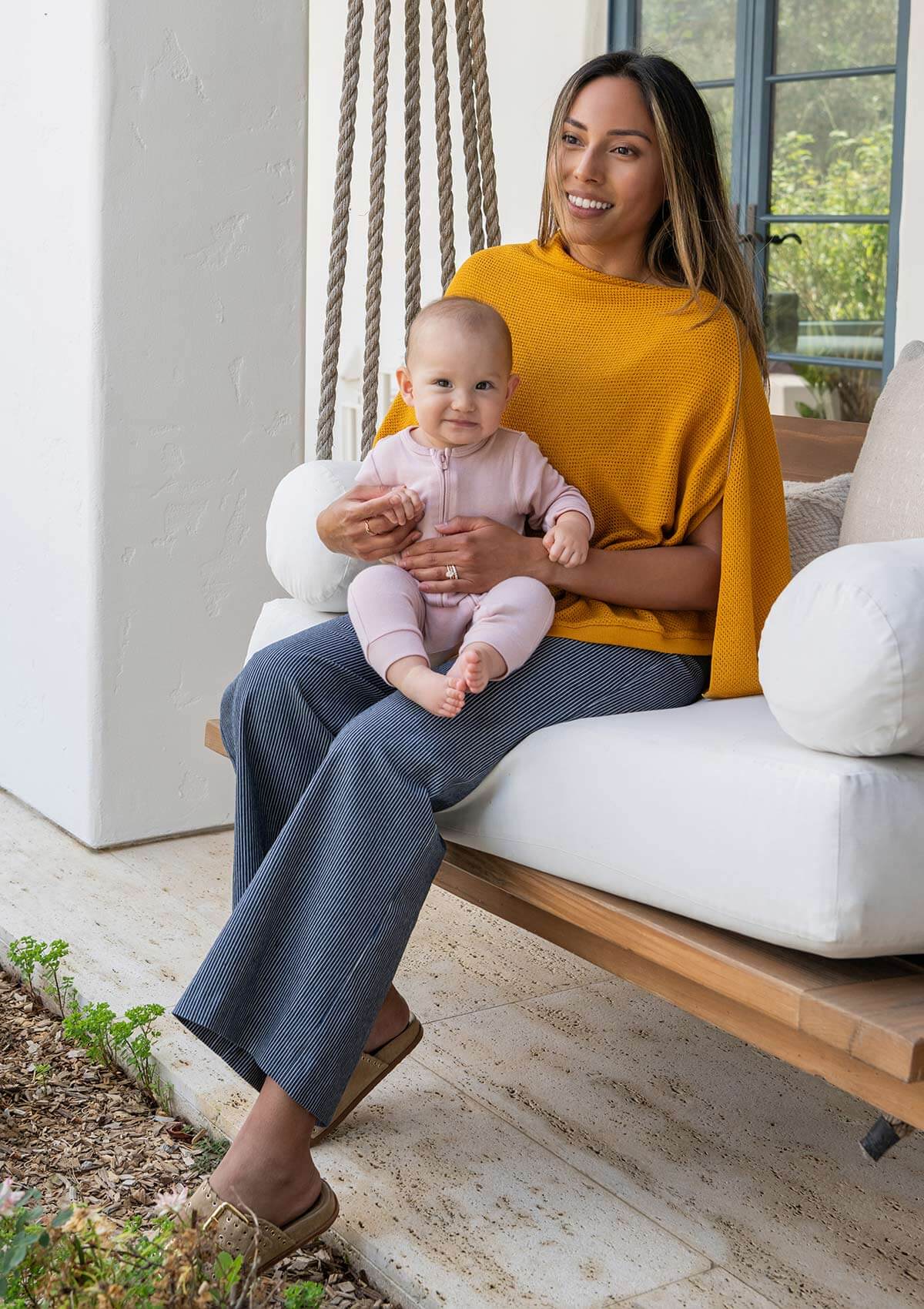 Mother in yellow top sitting with smiling baby on modern hanging swing chair