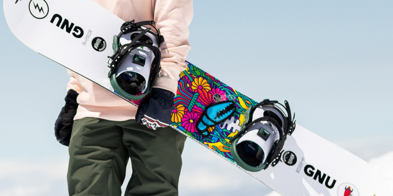 Snowboarder holding colorful board with GNU logo against sky