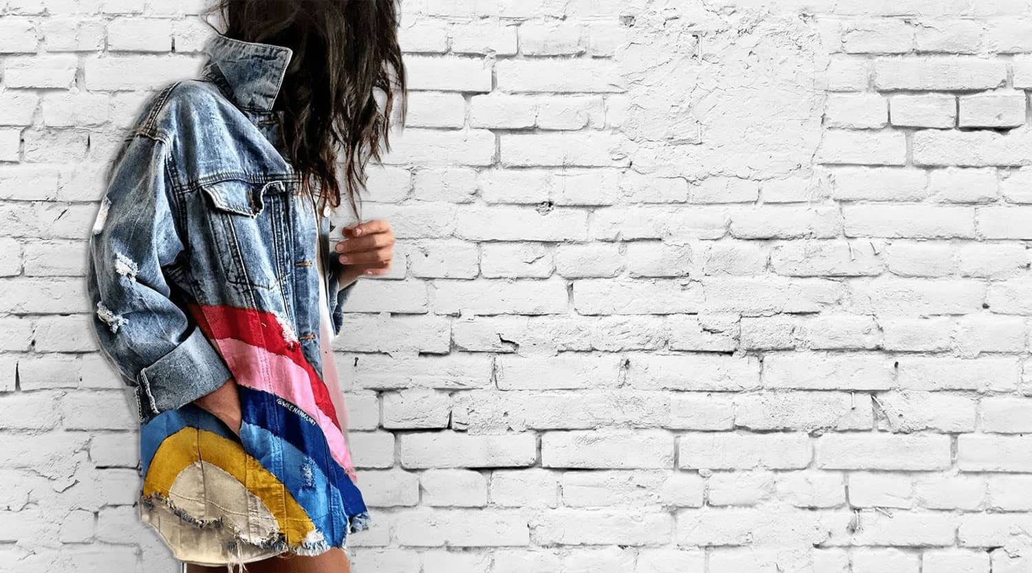 Denim jacket with colorful rainbow stripes against white brick wall