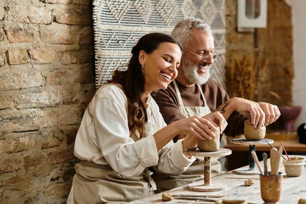 Two people smiling while working together on pottery wheel