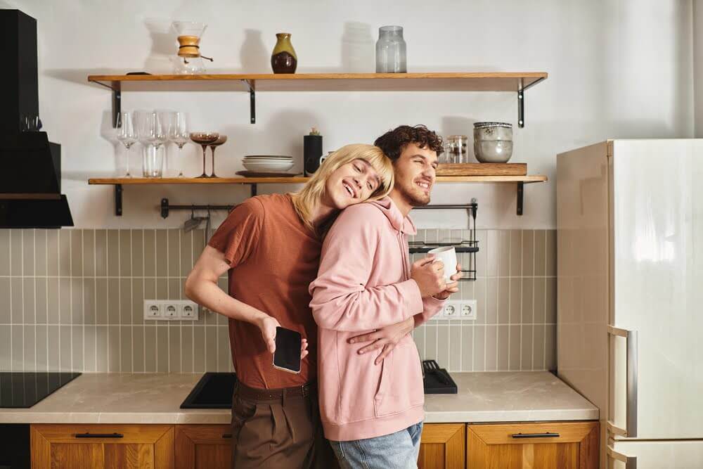 Couple hugging in kitchen, leaning on each other with warm smiles