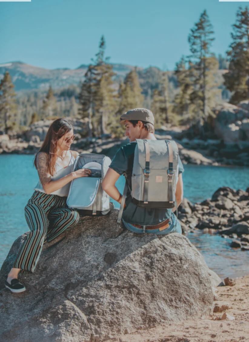 Two hikers sitting on a rock by a lake with pine trees and mountains