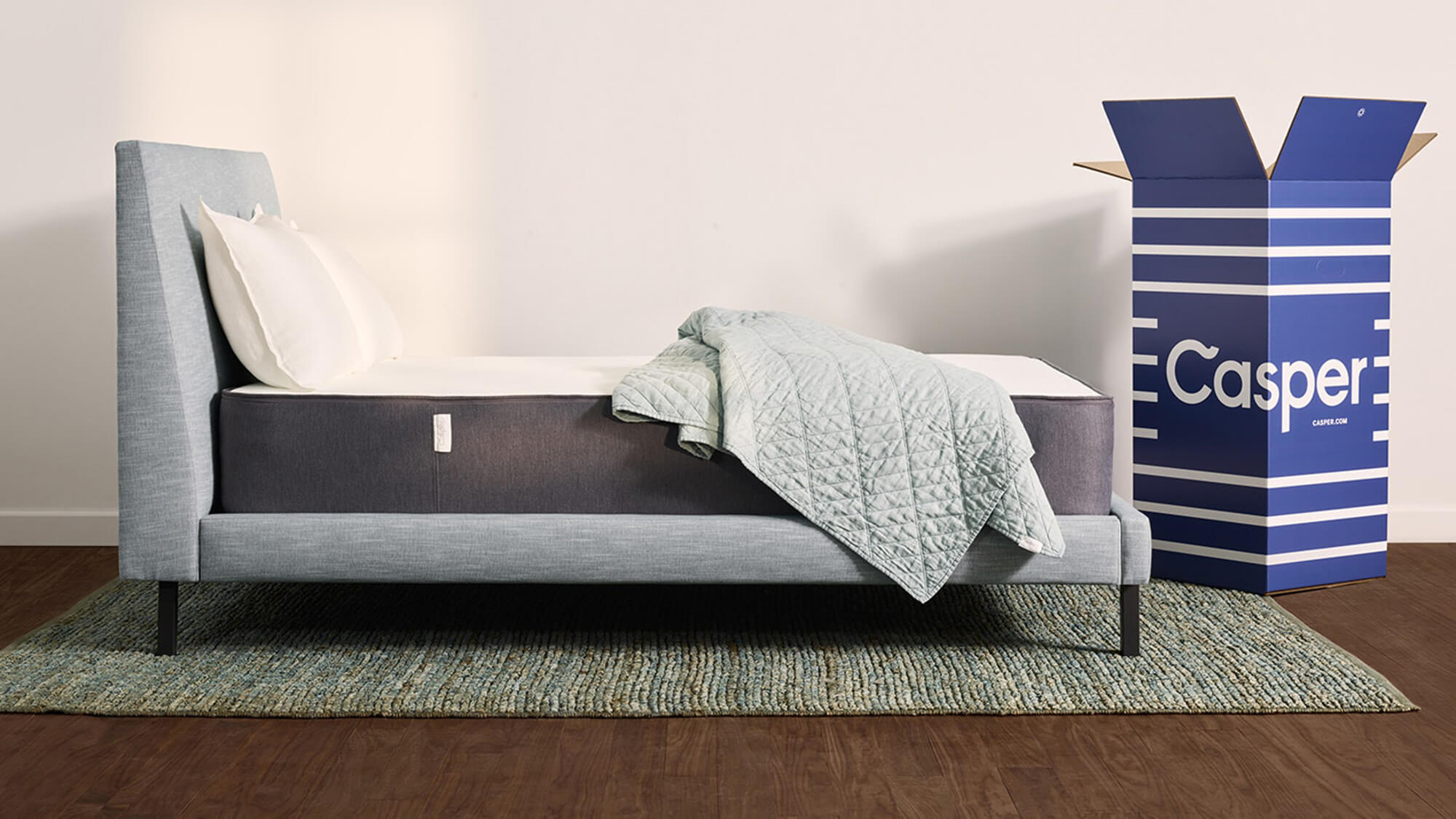 Casper mattress on gray bed frame with blue shipping box beside it