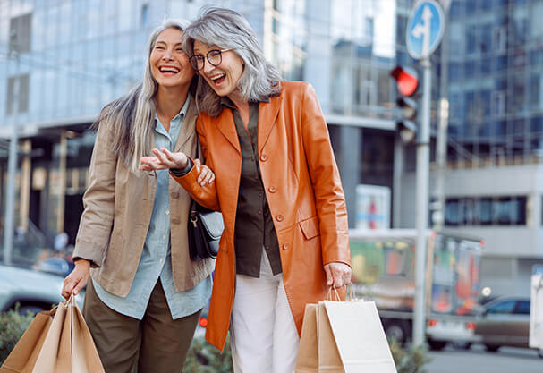 Two women laughing while shopping together in urban city street