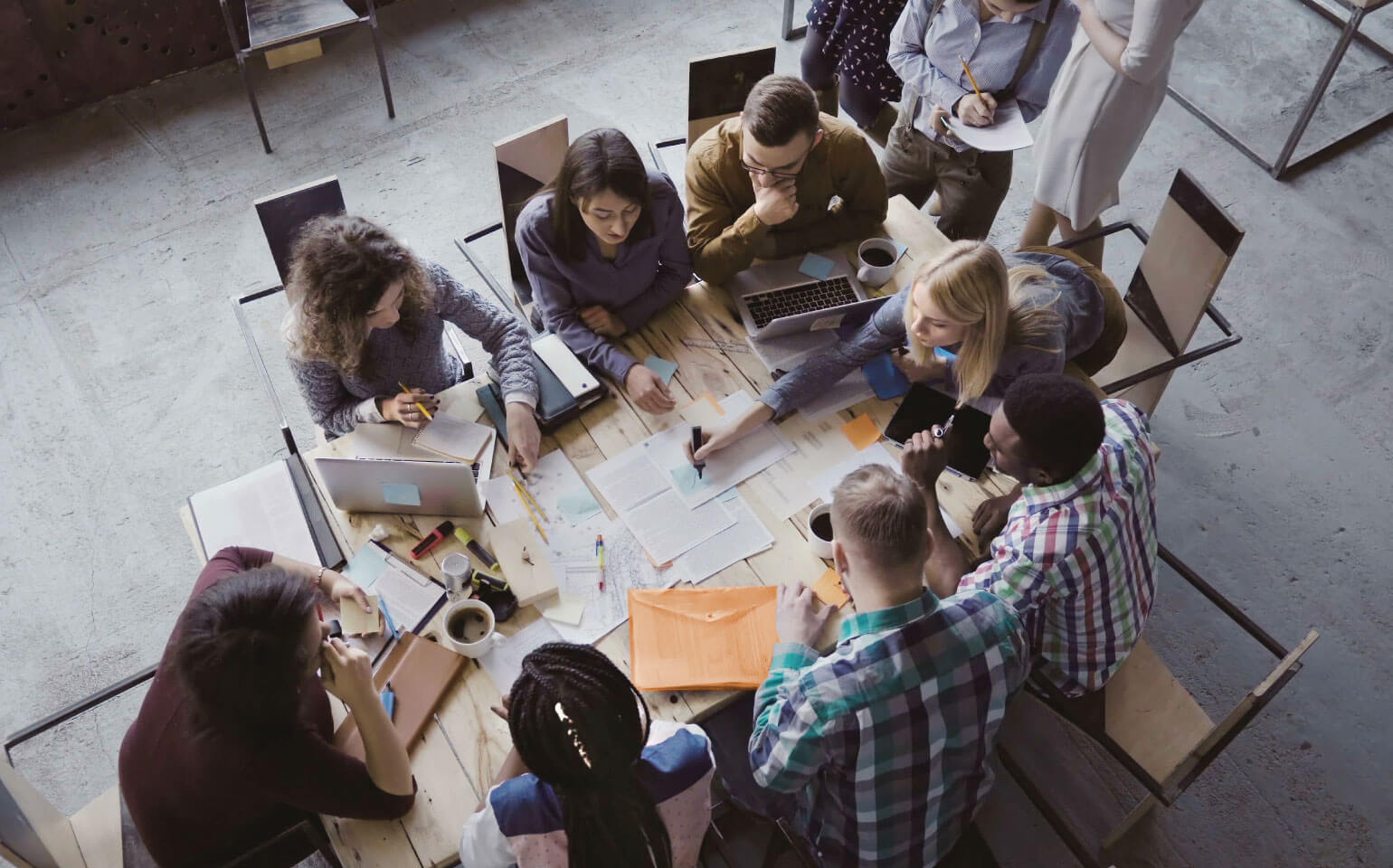 Diverse team collaborating around table with laptops and documents