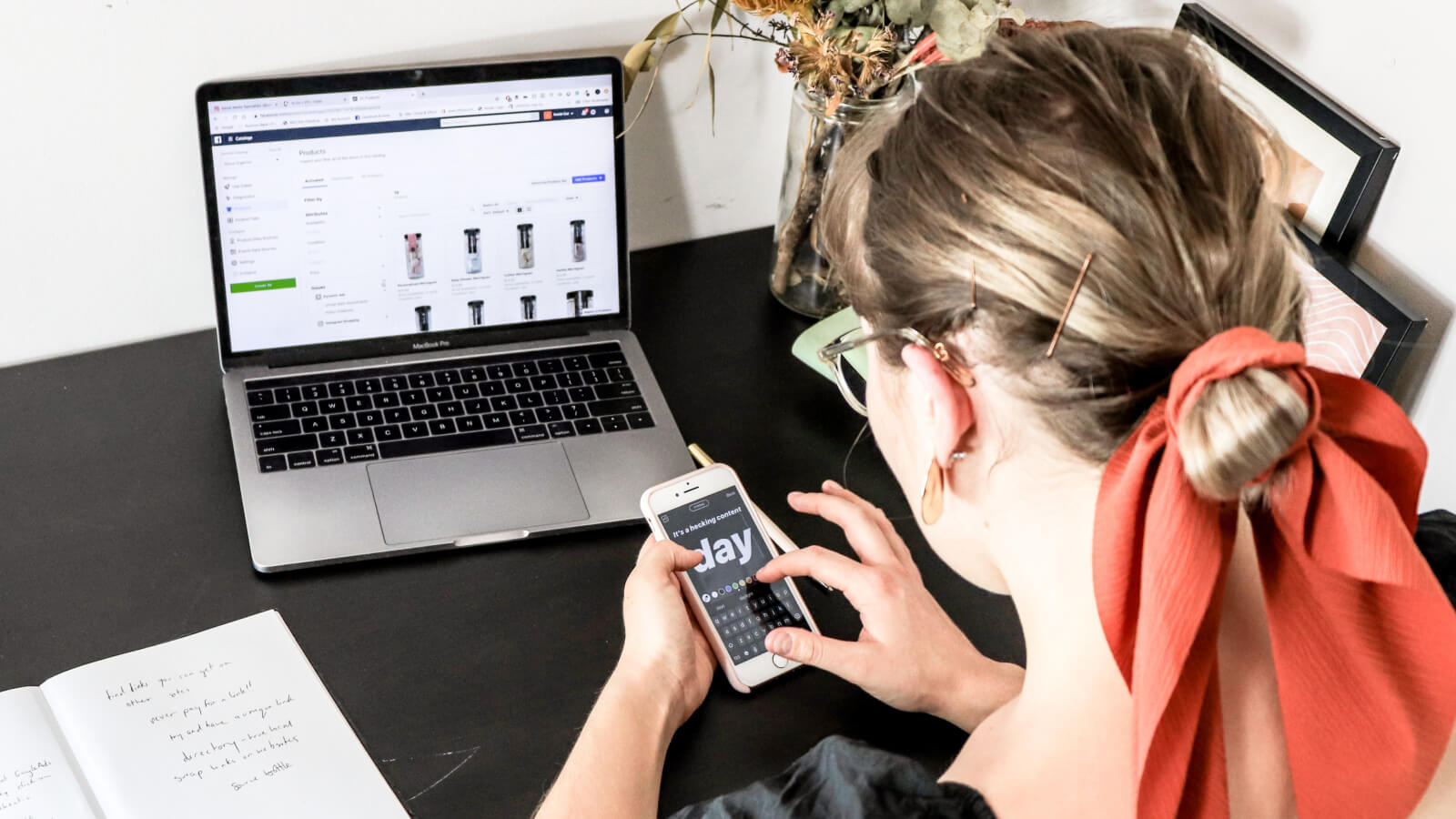 Person working on laptop and smartphone at desk with notebook