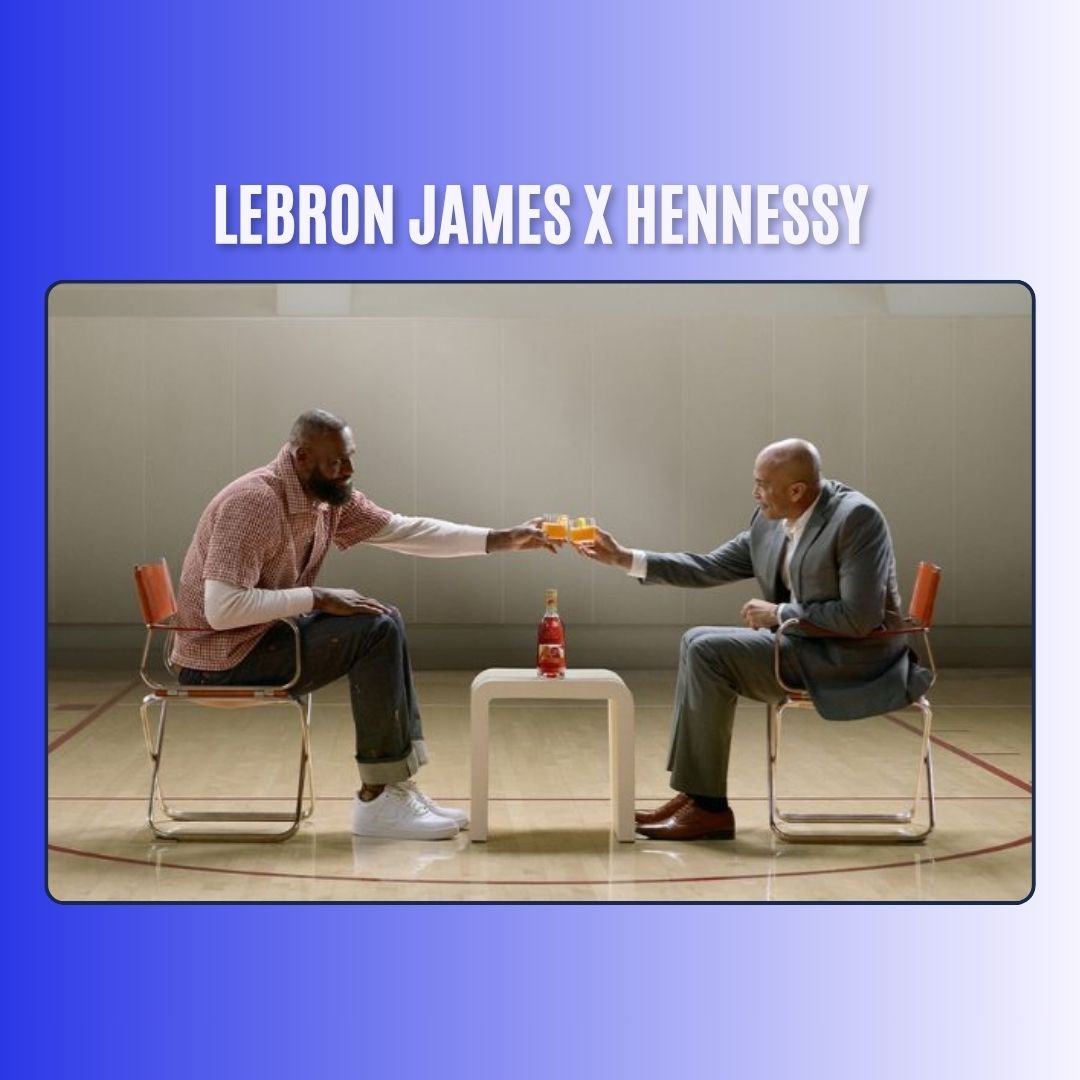 Two men toasting glasses of Hennessy while sitting on chairs