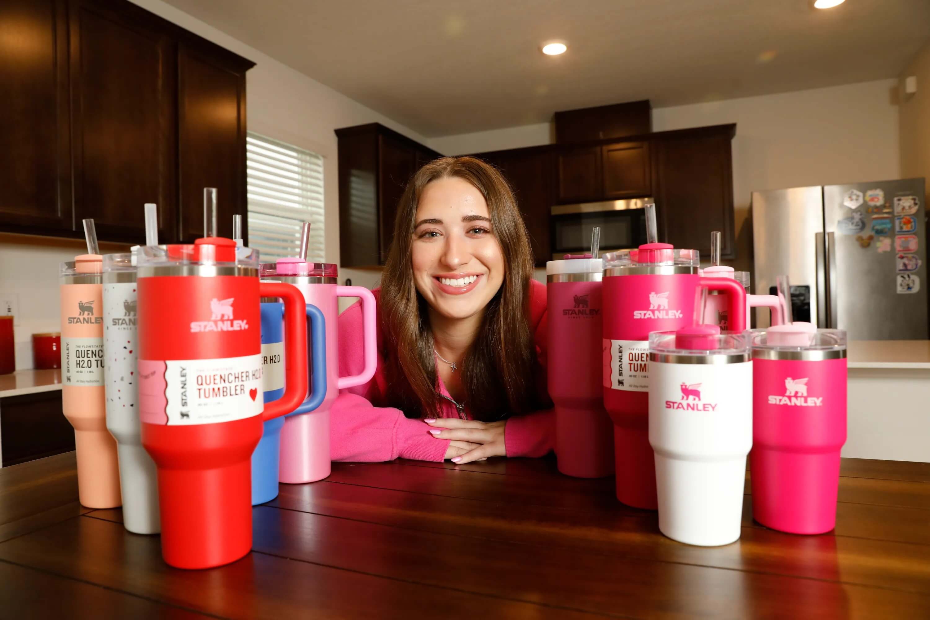 Smiling person with multiple colorful Stanley tumblers in kitchen