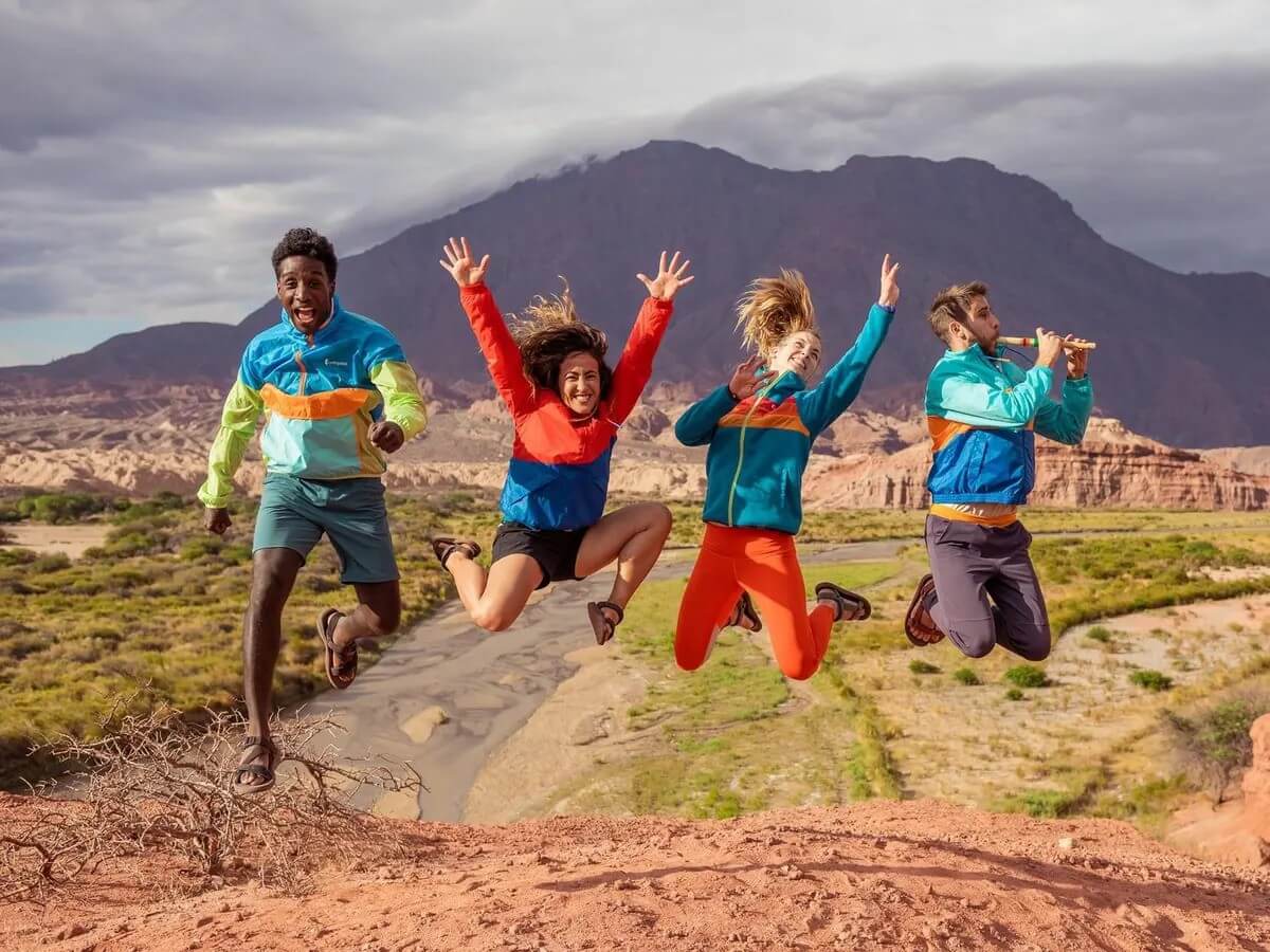 Four adventurers jumping with joy in colorful jackets near desert mountain