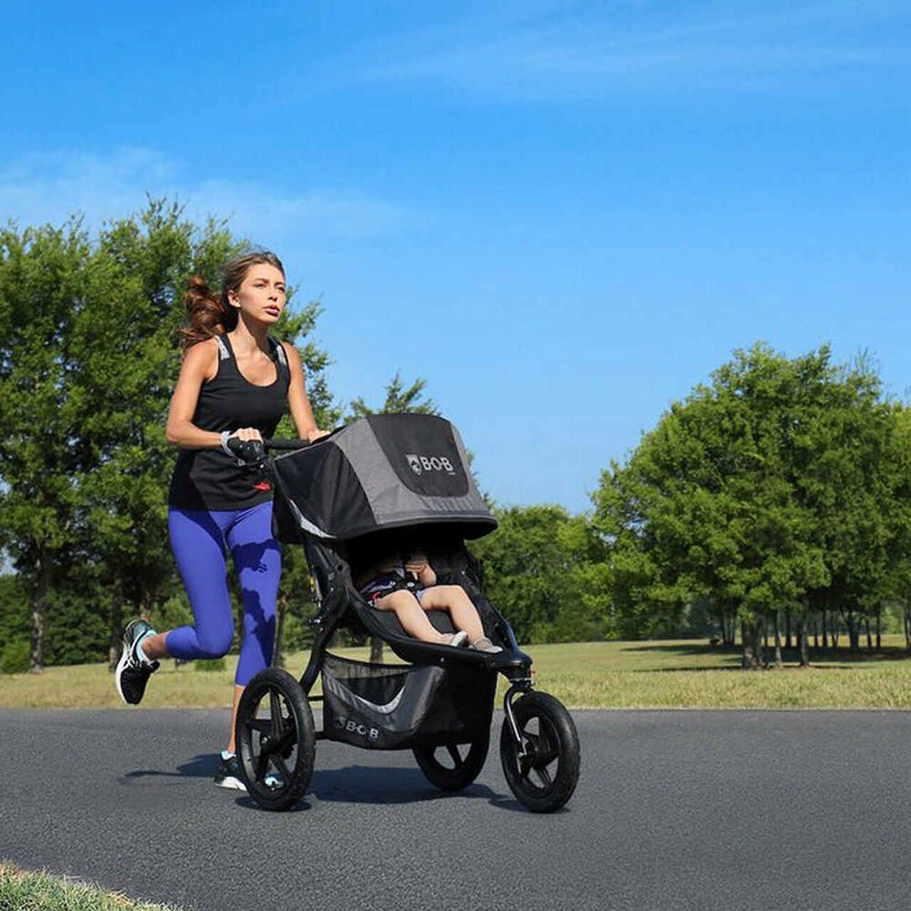Woman jogging with child in BOB stroller on sunny park path