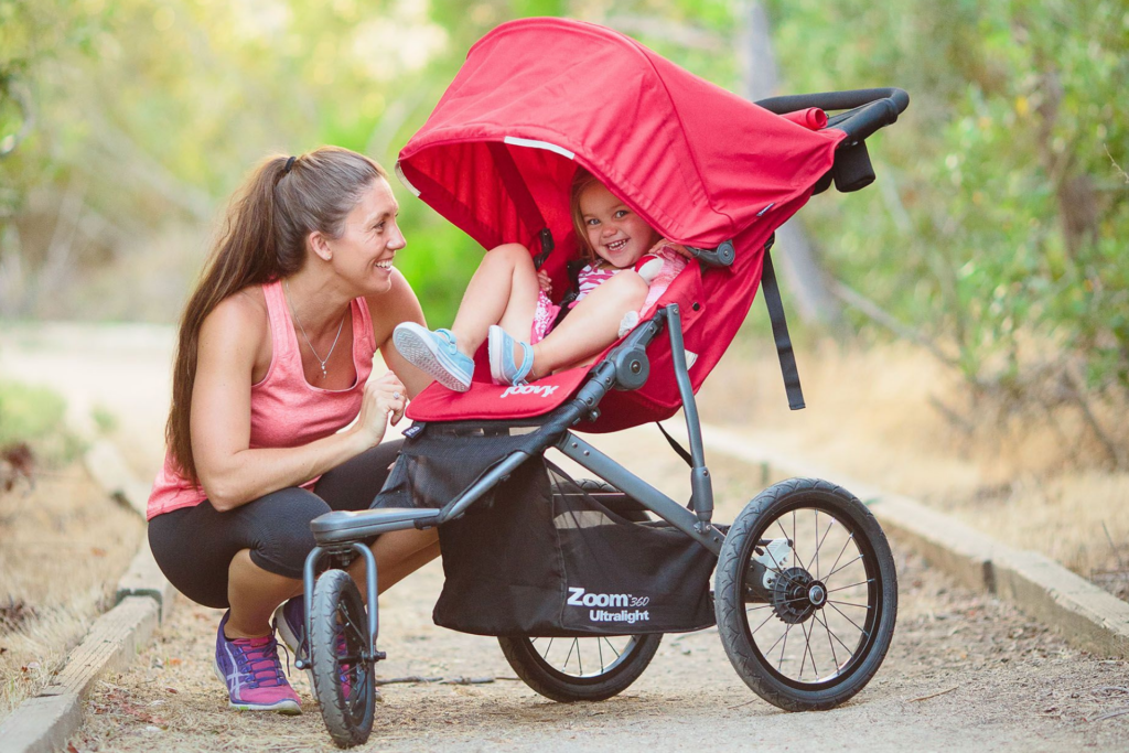Smiling mother with child in bright red jogging stroller outdoors