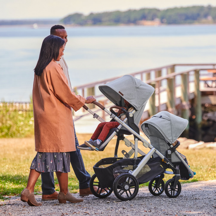 Parents pushing two strollers along waterfront path on sunny day