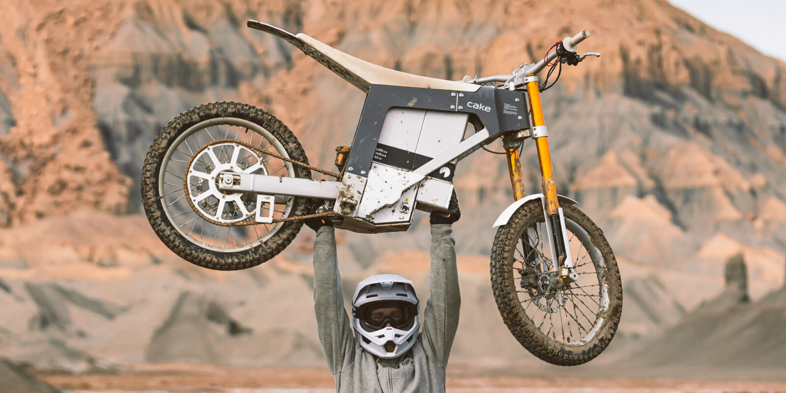 Dirt bike lifted overhead in rocky desert landscape with rider's helmet