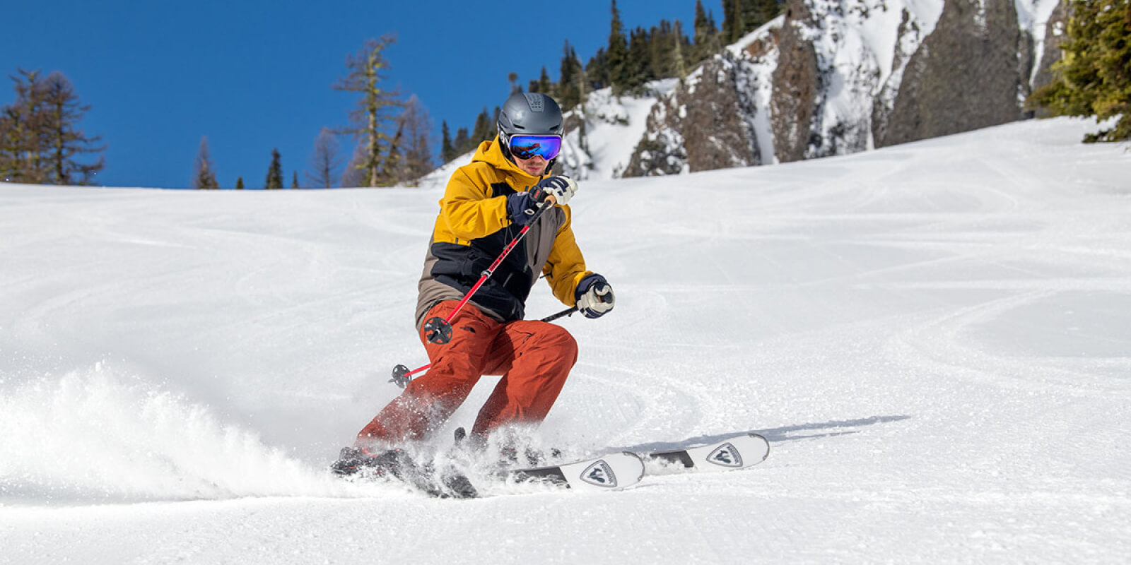 Skier in yellow jacket and red pants skiing down snowy mountain slope