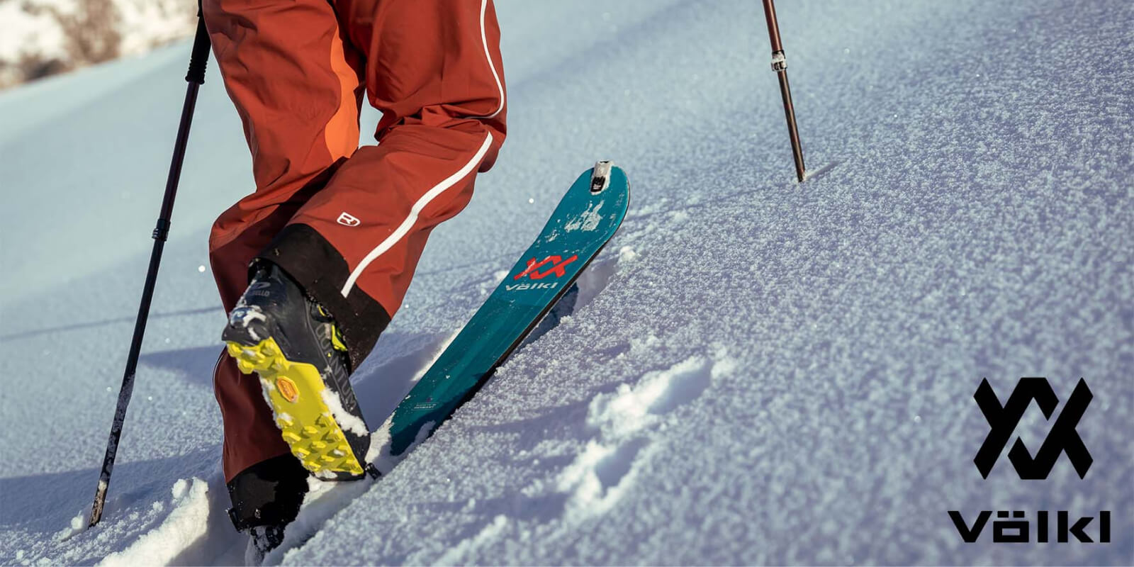 Skier in red pants gliding on a teal Völkl ski through fresh snow