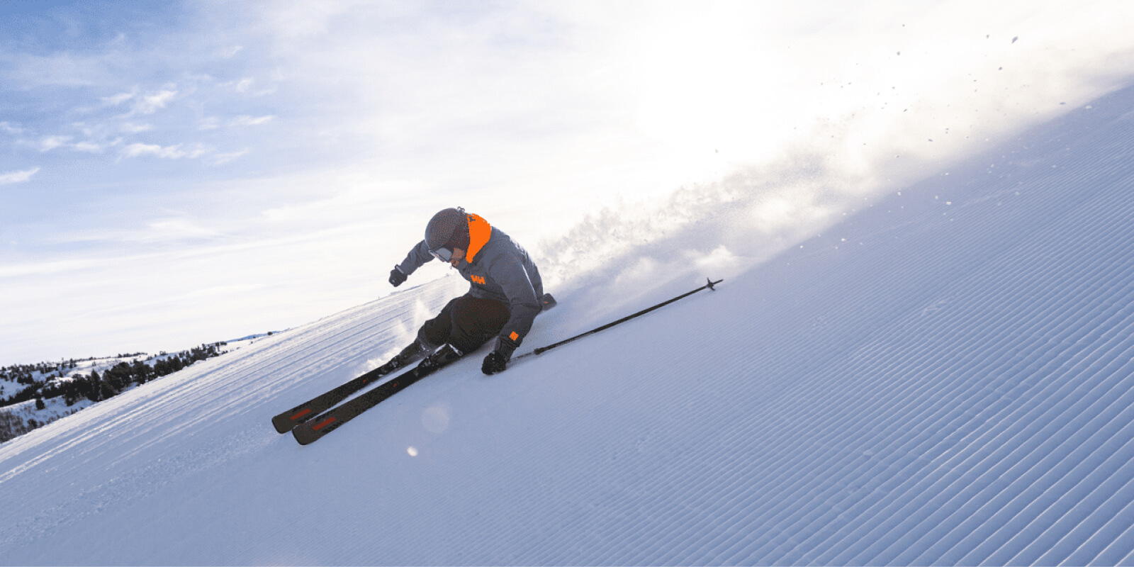 Skier in orange and gray carving down a snowy mountain slope