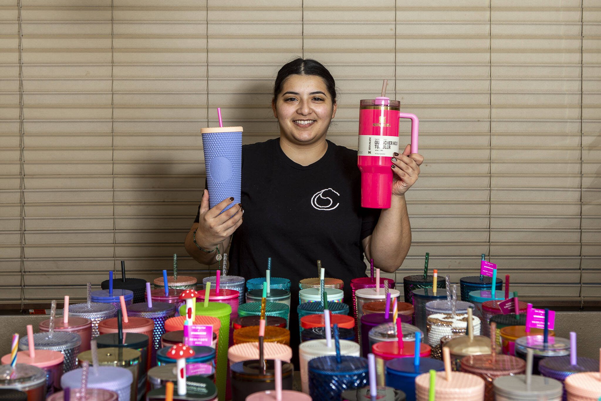 Smiling person with colorful collection of tumbler cups and drinking straws