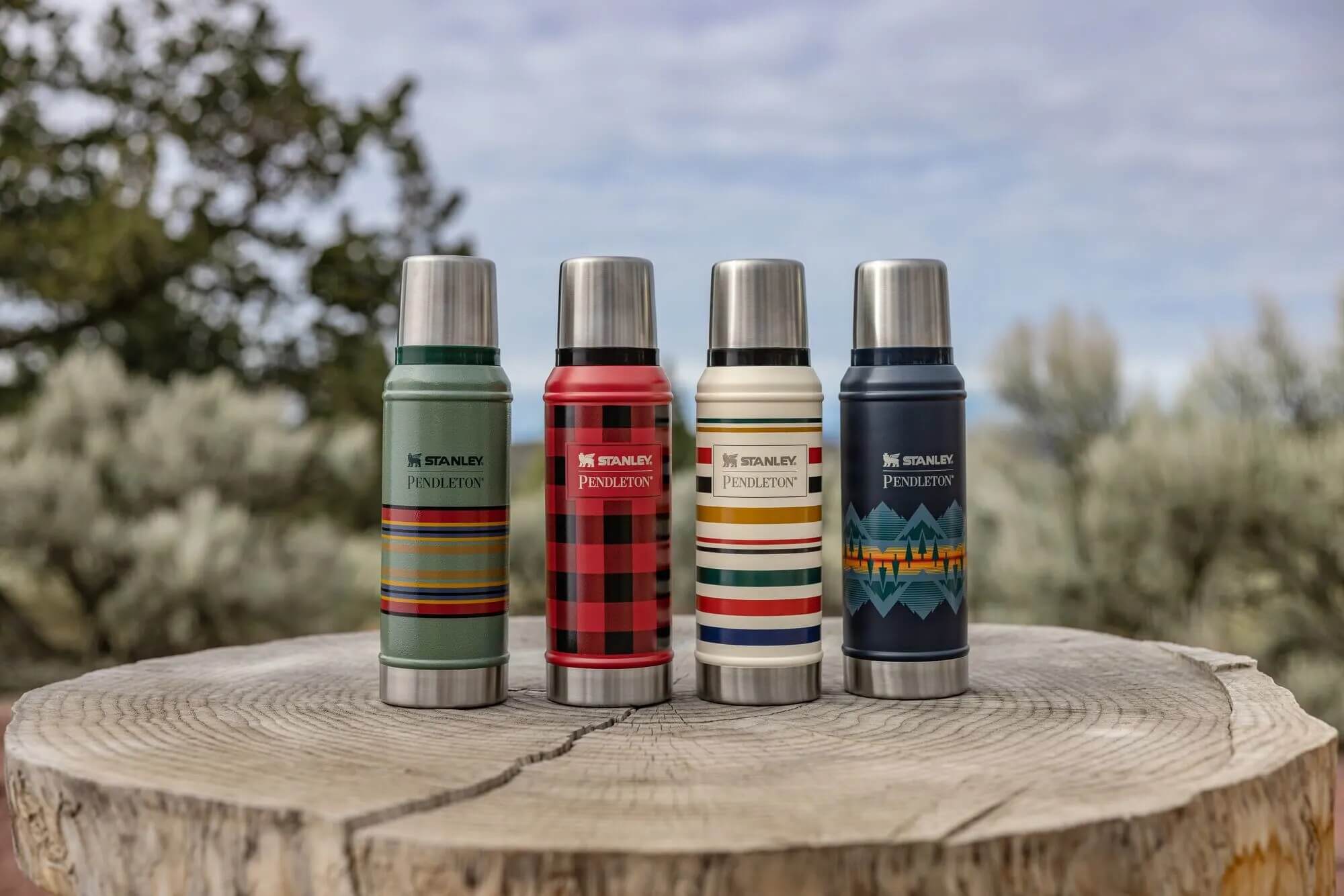 Four Stanley Pendleton thermoses with unique patterns on a wooden log
