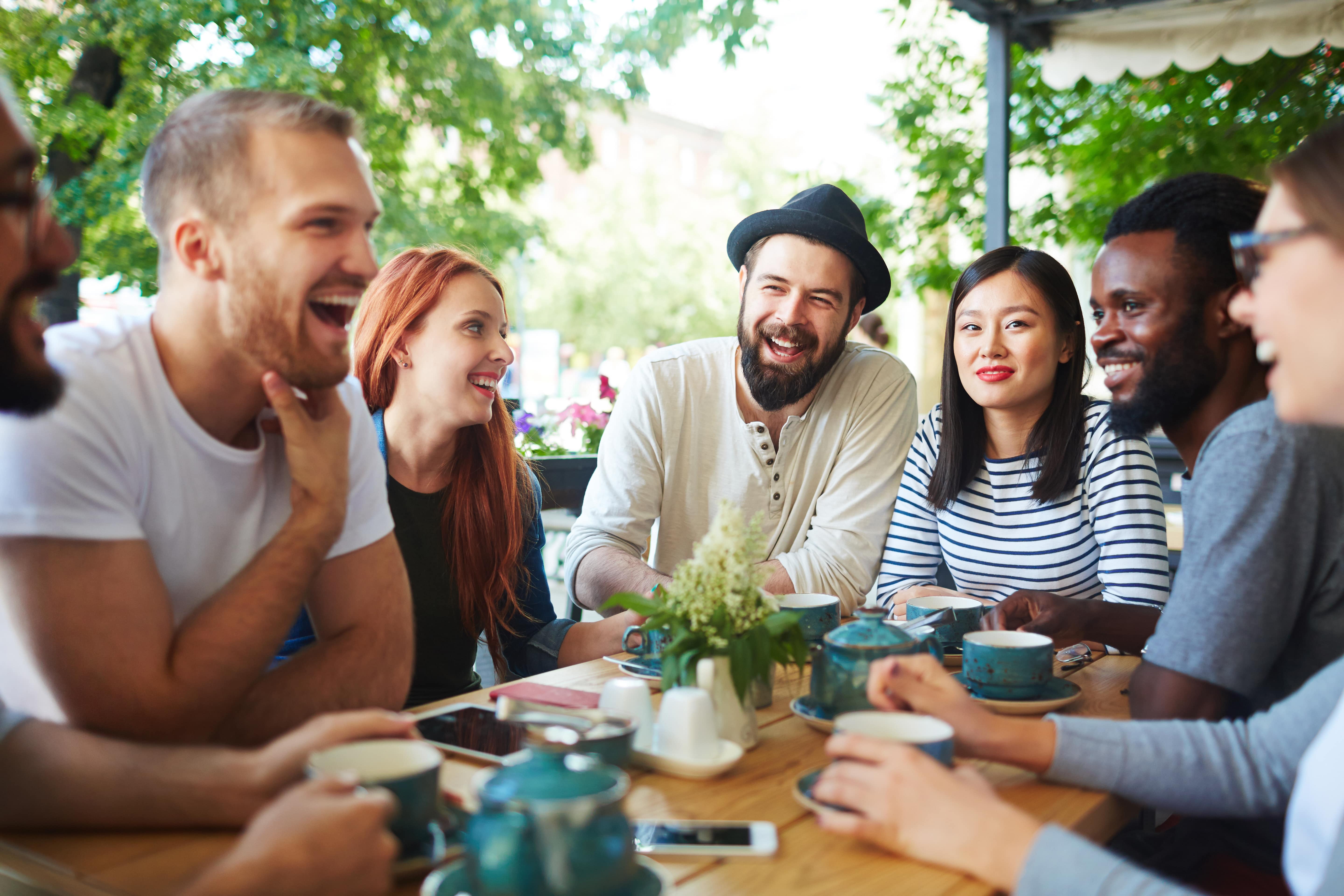 Diverse group of friends laughing and enjoying coffee together outdoors