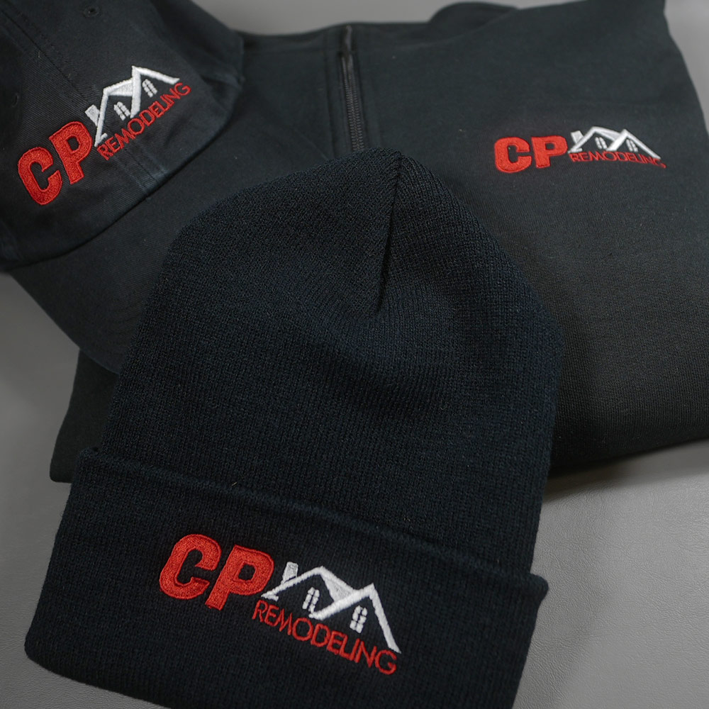 Black zip-up hoodie, baseball cap, and knit beanie with red and white CP Remodeling embroidered logo featuring house roofs.