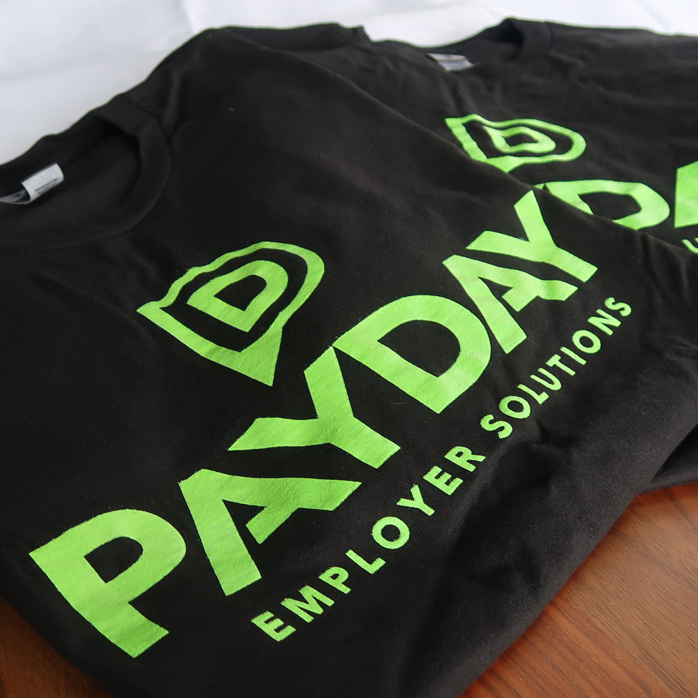 Two black T-shirts with bright green text and logo reading 'PAYDAY EMPLOYER SOLUTIONS' 