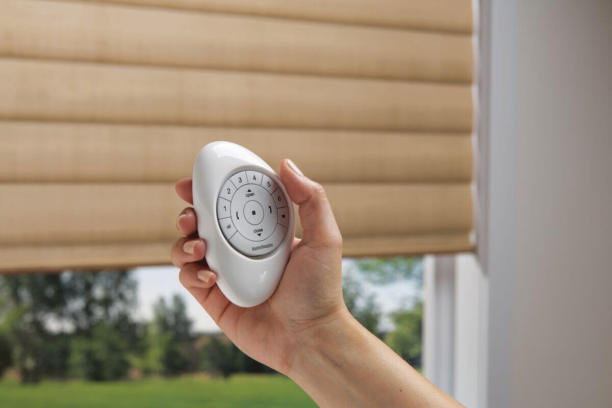 Hand holding remote for motorized blinds.