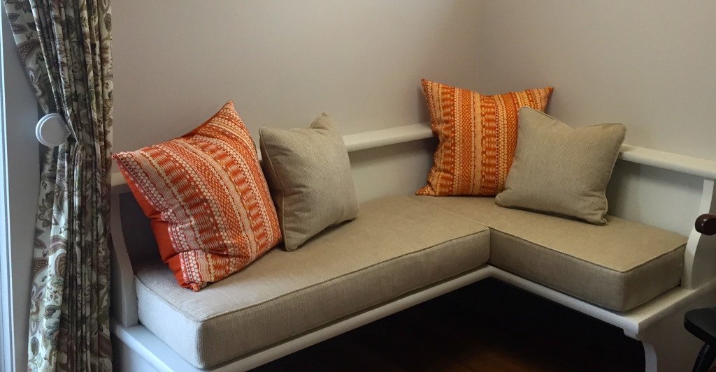 Corner bench with beige cushions and orange-patterned pillows.
