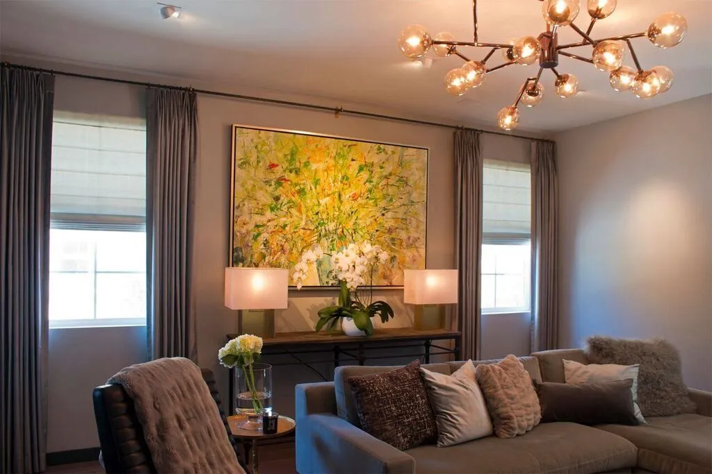 Living room with gray drapes, sofa, modern chandelier, large floral art.
