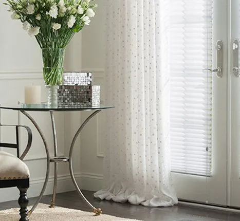 Glass table, white drapes, and flowers near glass door.