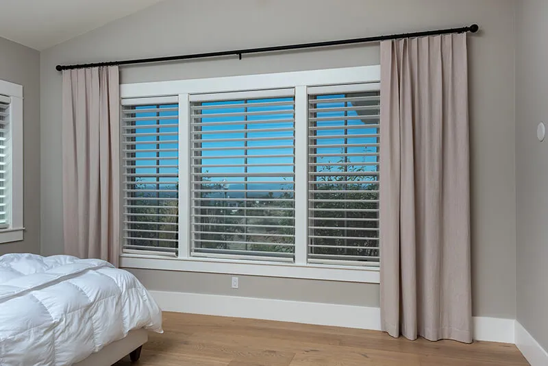 Bedroom window with striped shades and beige curtains.