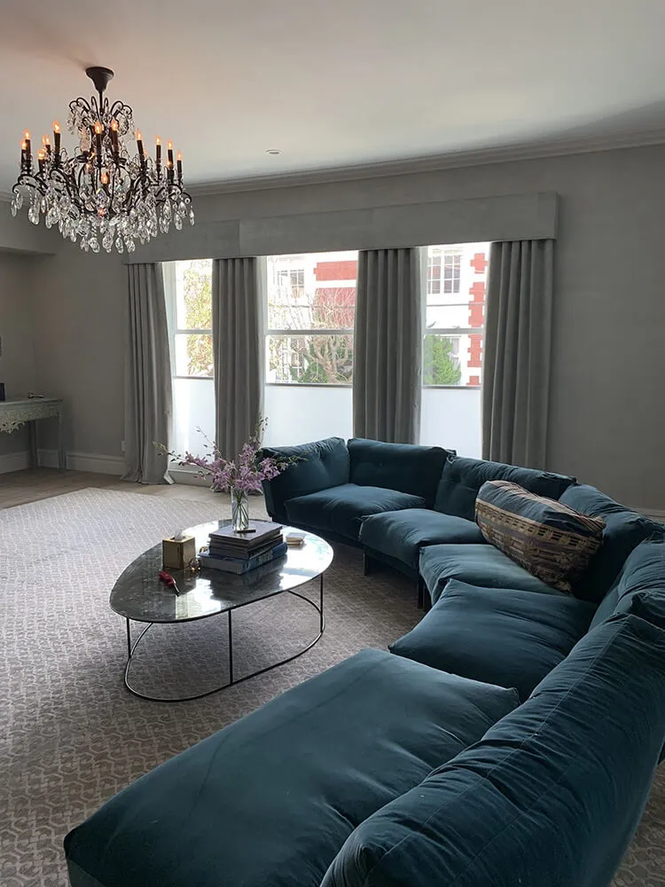 Elegant living room with blue sectional, chandelier, and large drapes.