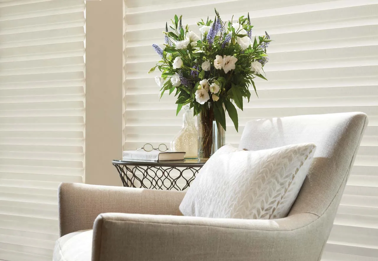 Armchair next to cellular shades with a flower vase.