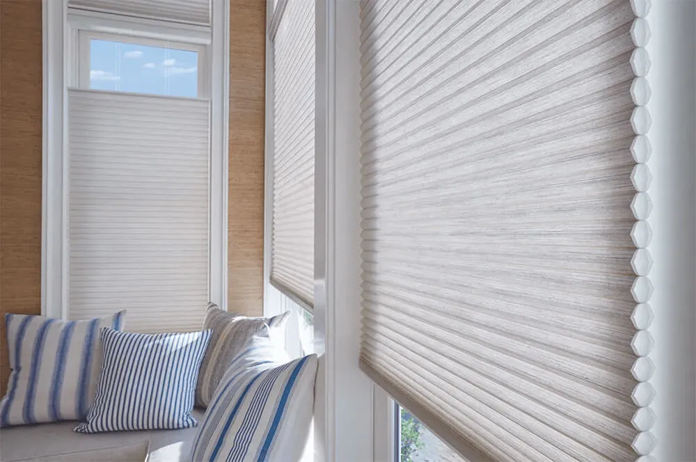 Cellular honeycomb shades in cozy room with blue-striped pillows.