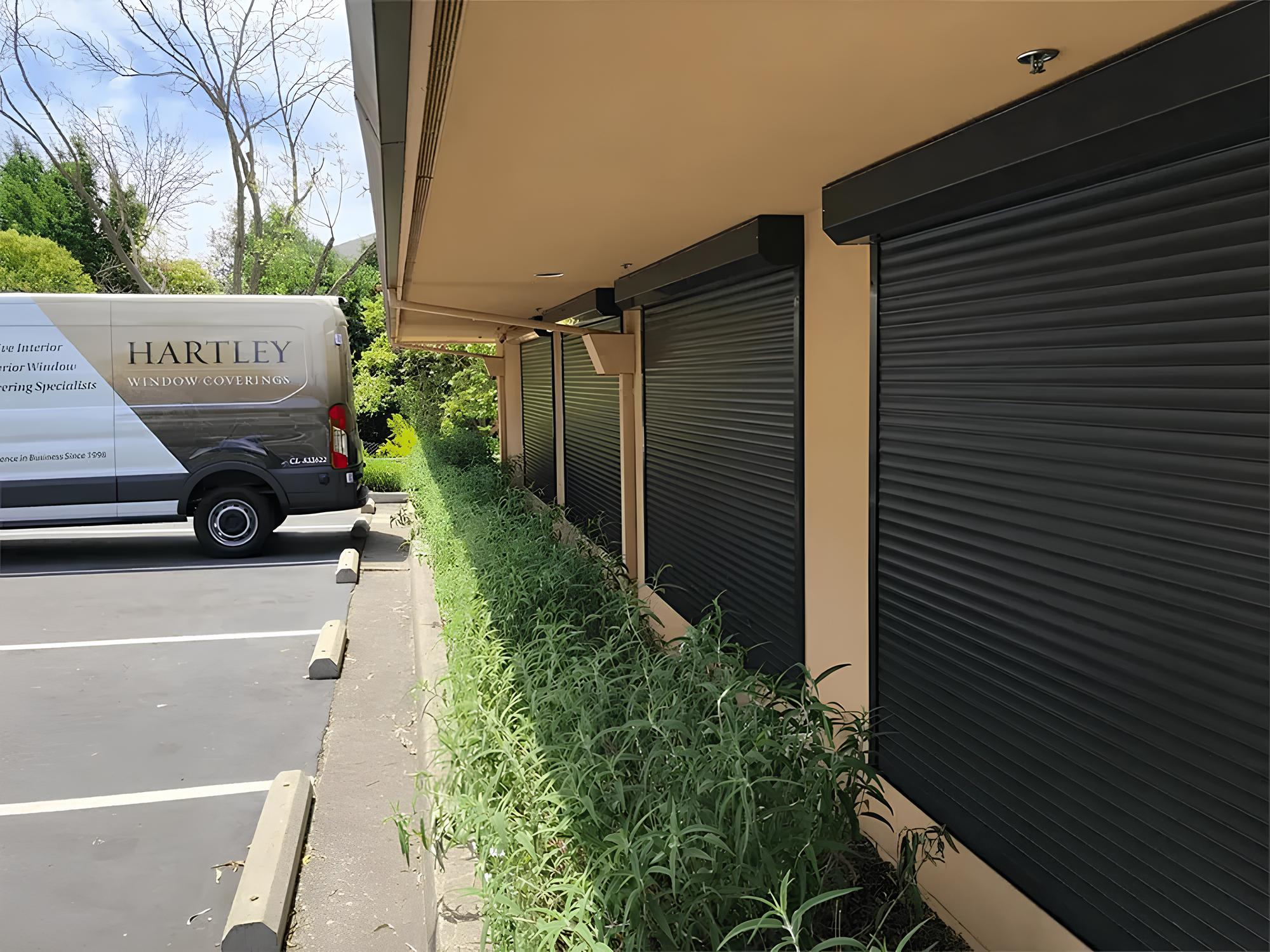 Rolling shutters on building exterior, Hartley Window Coverings van in parking lot.
