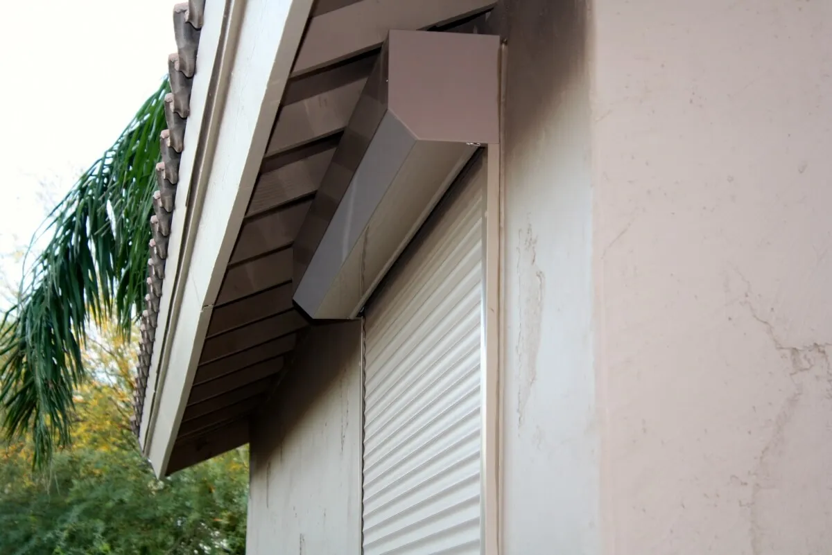 Exterior rolling shutter on beige house facade under a sloped roof.