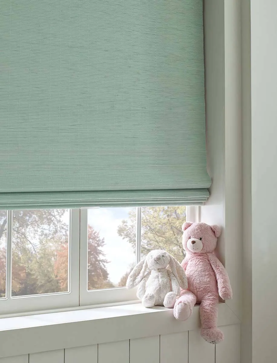 Woven wood shade over window with pink and white plush toys on sill.