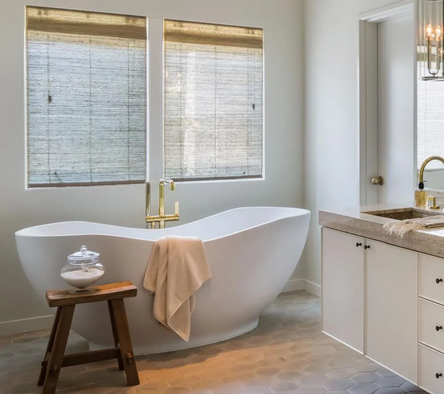 Elegant bathroom with freestanding tub, wooden stool, and woven wood shades.