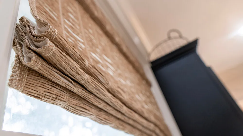 Woven wood shades partially open on window.
