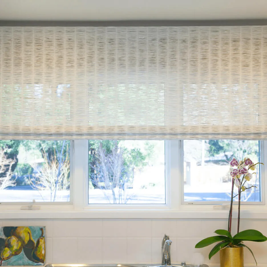 Woven wood shades above kitchen window with orchid plant.