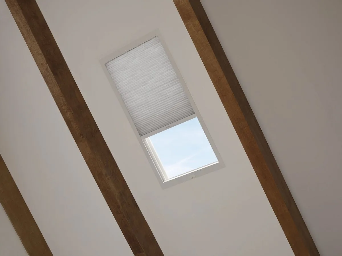 Skylight with shade partially closed on slanted ceiling.
