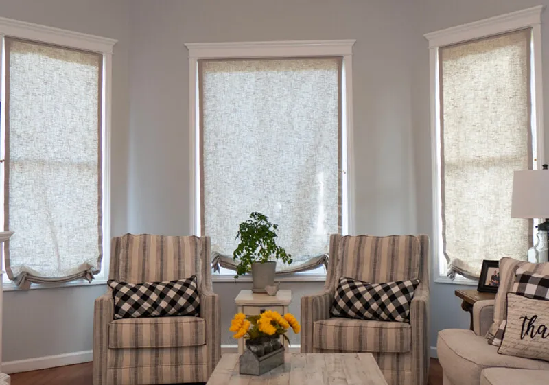 Living room with beige Roman shades behind armchairs.