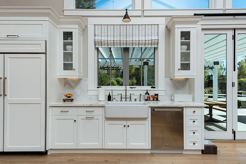 Elegant kitchen with striped Roman shade above sink.