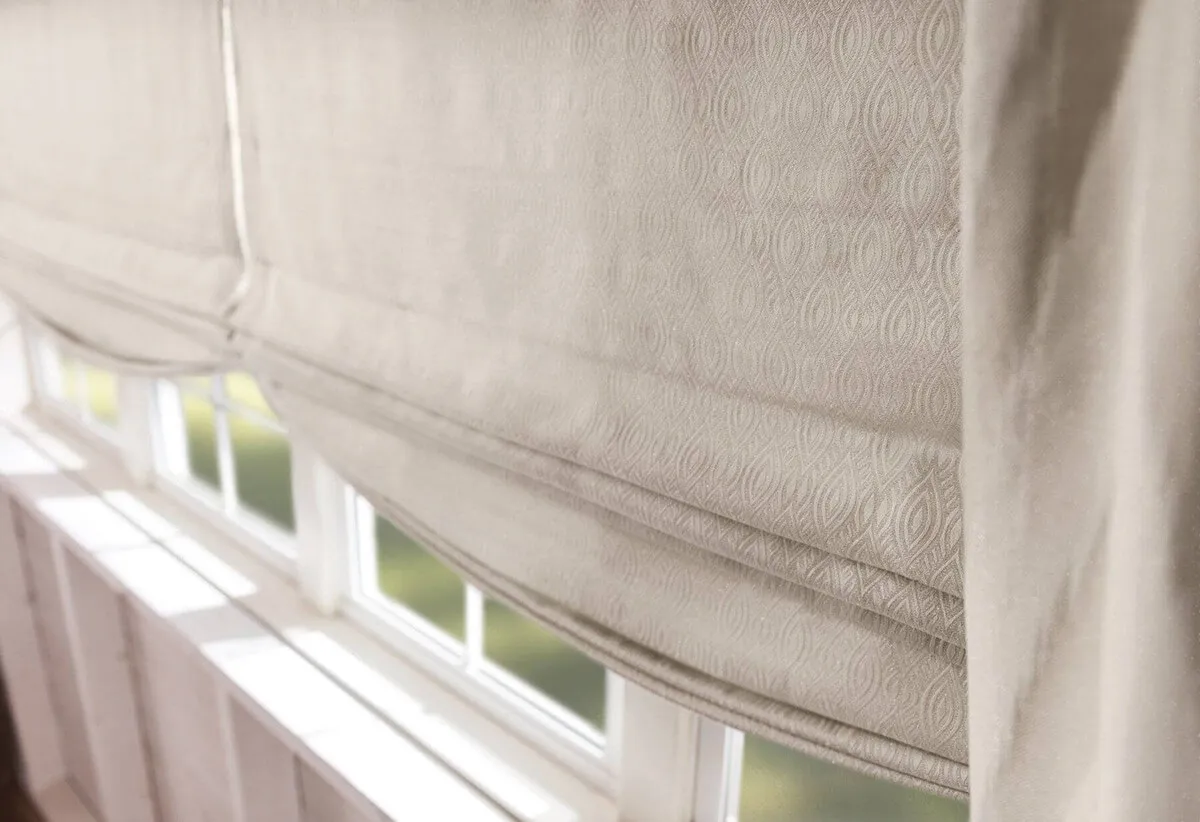 Close-up of beige Roman shades on windows.
