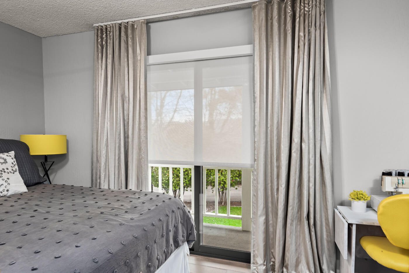 Bedroom with roller shade, curtains, bed, desk, and chair.