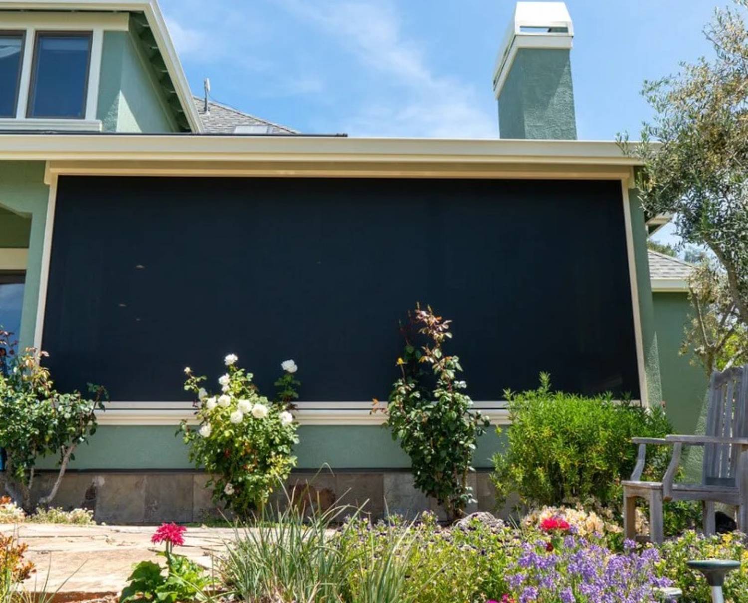 Retractable patio screen covering a window on a green house, surrounded by a colorful garden.