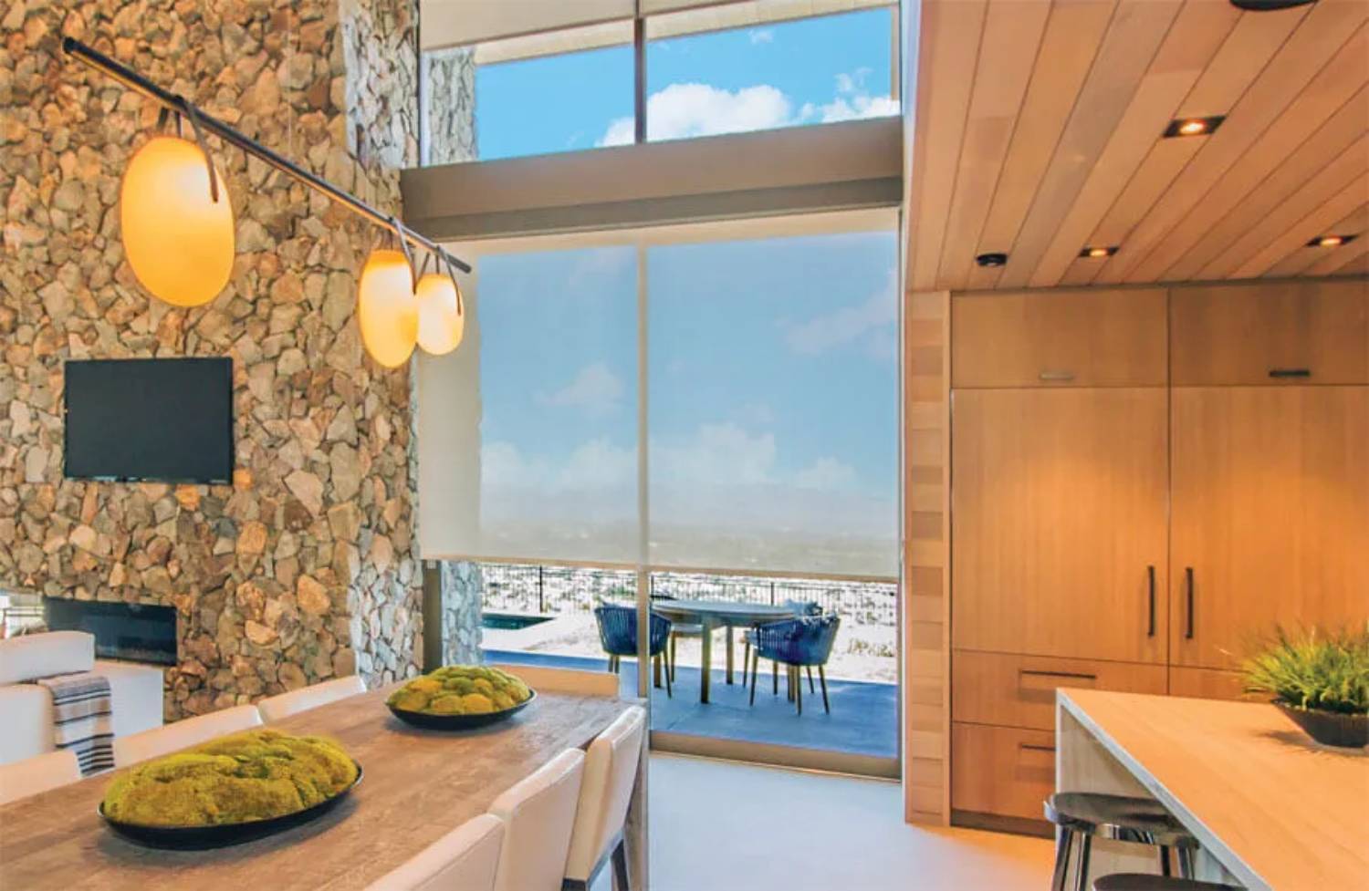 Modern kitchen and dining area with stone wall and large windows.