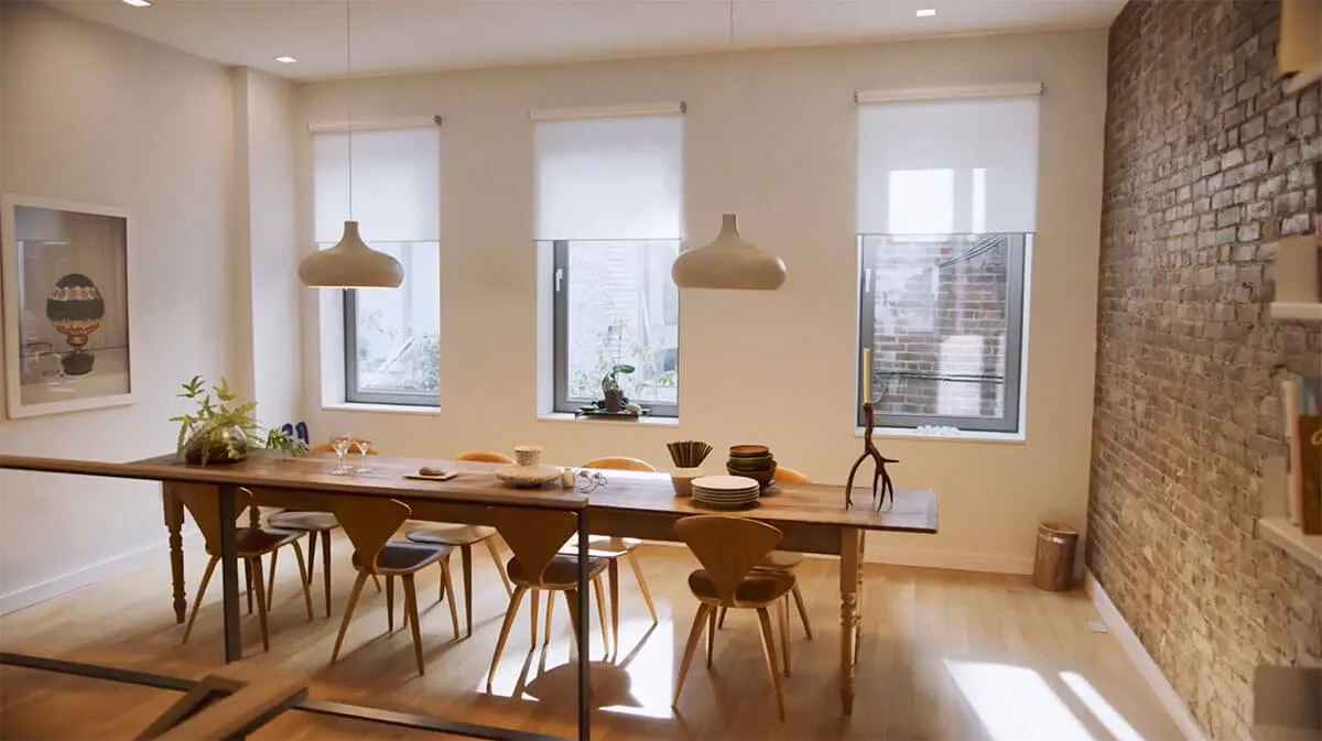 Modern dining room with a long wooden table and three windows.